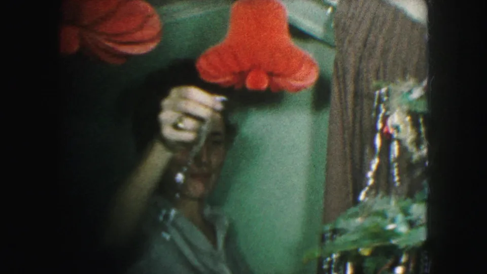 1959 Kansas City home-movie frame with a partly visible face near red hanging decorations and the edge of a Christmas tree.