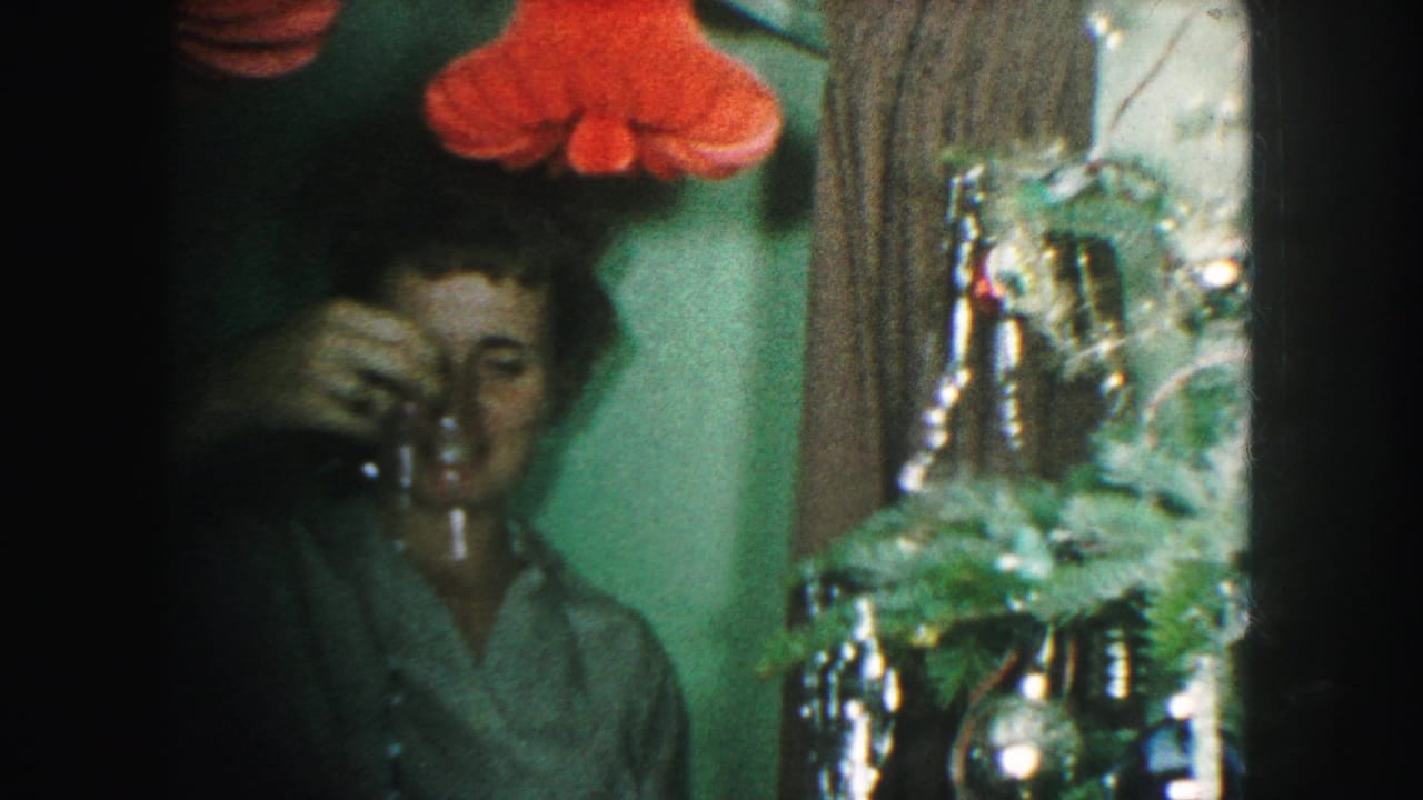 Woman reaches toward her face or the tree while standing beside shiny ornaments and tinsel.