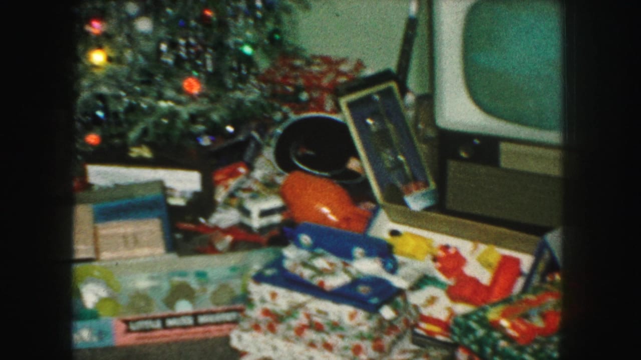 1959 Kansas City home-movie frame showing a Christmas tree, wrapped presents, toy packaging, and a boxy television nearby.
