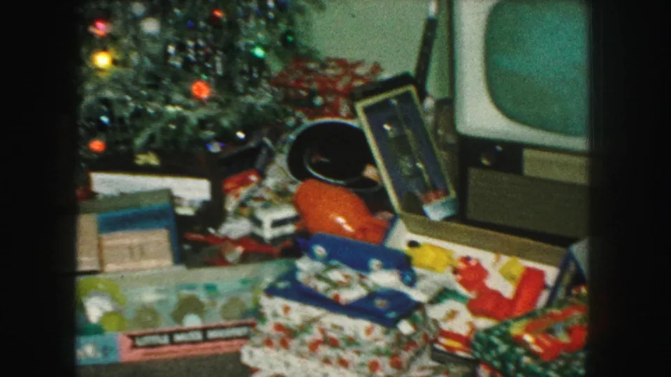 1959 Kansas City home-movie frame showing a Christmas tree, wrapped presents, toy packaging, and a boxy television nearby.