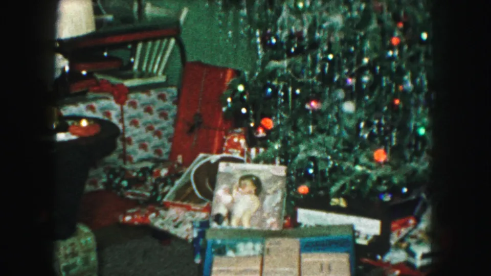 1959 Kansas City home-movie frame centered on a tinsel-decorated Christmas tree with boxed toys and wrapped gifts below.