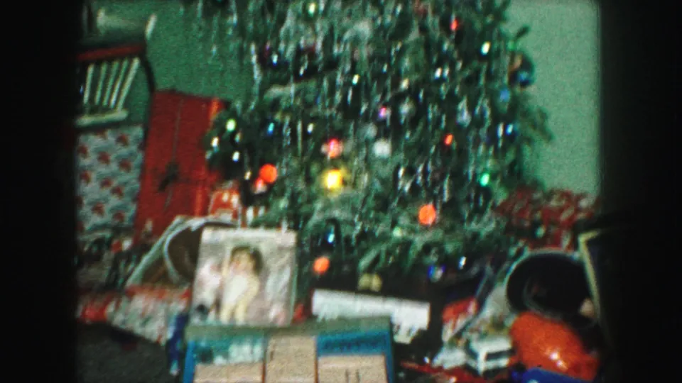 1959 Kansas City home-movie frame showing a decorated Christmas tree with silver tinsel, ornaments, gifts, and a framed photograph below.
