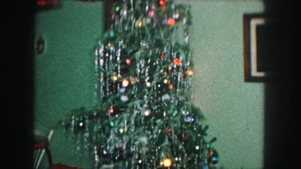 1959 Kansas City home-movie frame focused on the upper section of a Christmas tree with dense tinsel and bright ornaments.