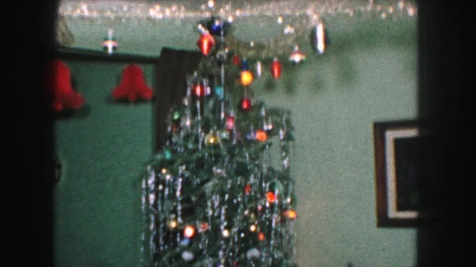 1959 Kansas City interior frame showing the top of a decorated Christmas tree beside red wall lamps and framed wall art.