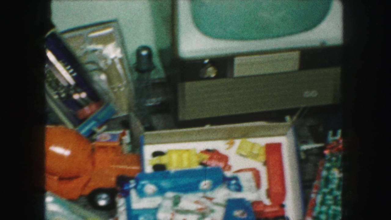 1959 Kansas City home-movie frame showing wrapped Christmas gifts, colorful toy vehicles, and a retro television in a private interior.