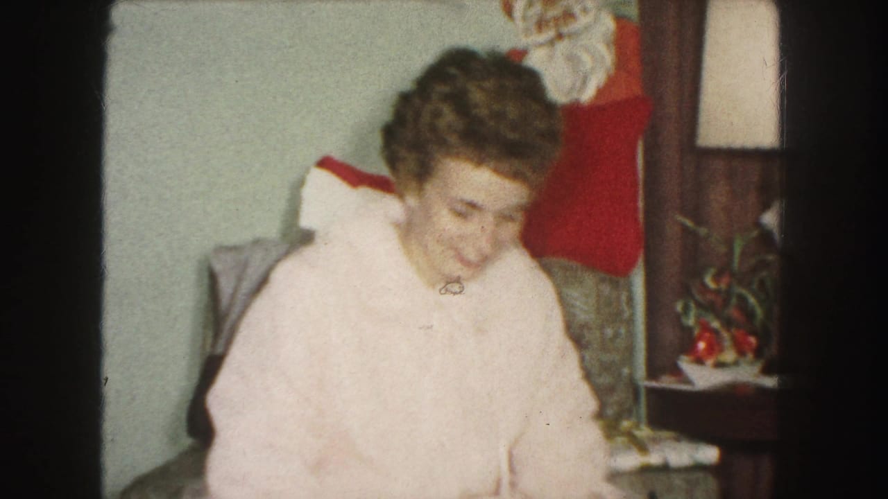 Woman in a pale pink robe sits near a side table and Christmas stocking.