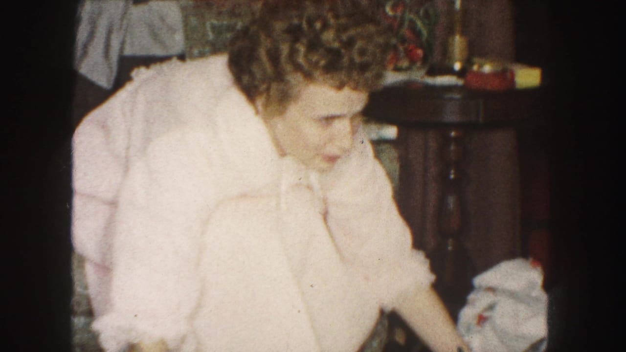 A woman in a pink robe reaches downward near loose paper in a 1959 Kansas City home decorated for Christmas.