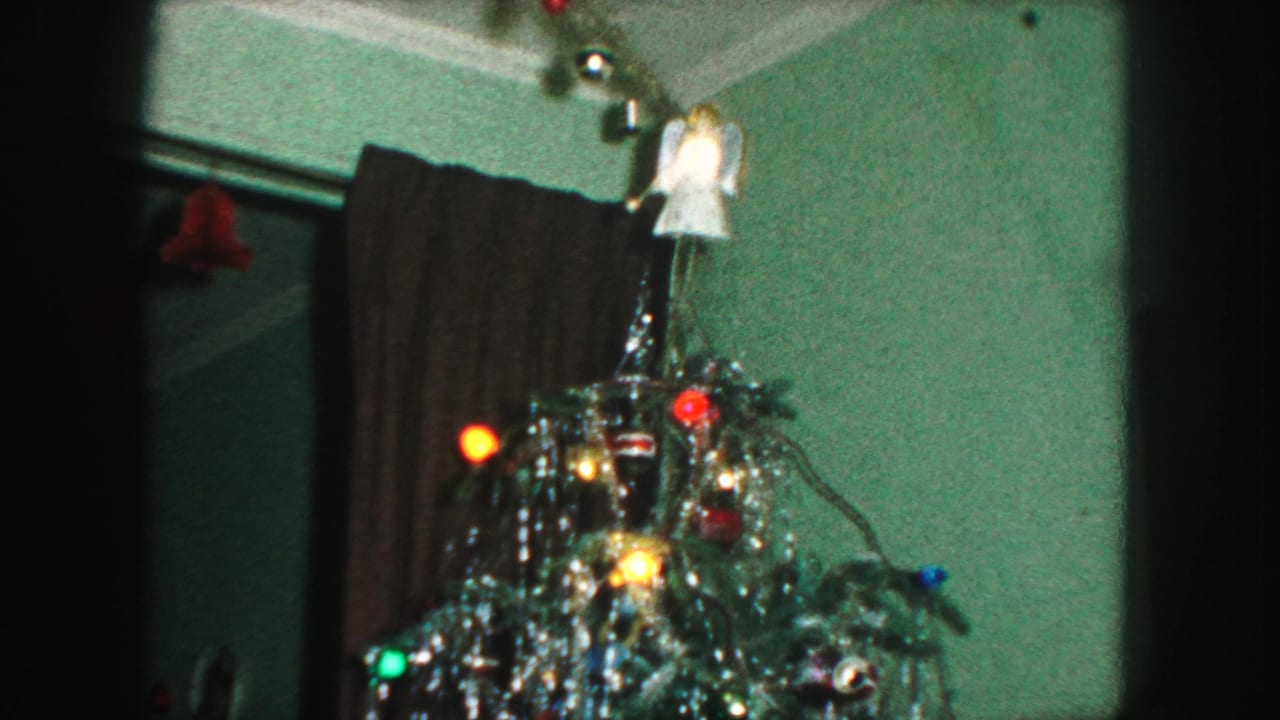 1959 Kansas City home-movie frame showing the upper Christmas tree with silver tinsel, colored lights, and an angel topper.