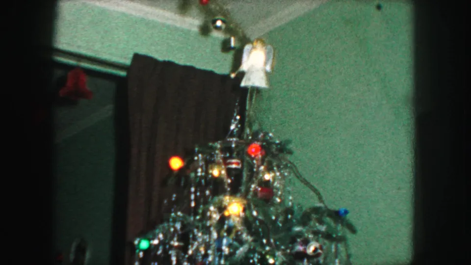 1959 Kansas City home-movie frame showing the upper Christmas tree with silver tinsel, colored lights, and an angel topper.