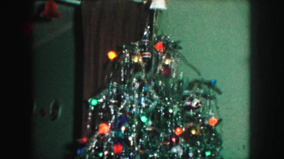 1959 Kansas City frame of a decorated Christmas tree beside a dark curtain, with colored lights and a pale angel at the top.