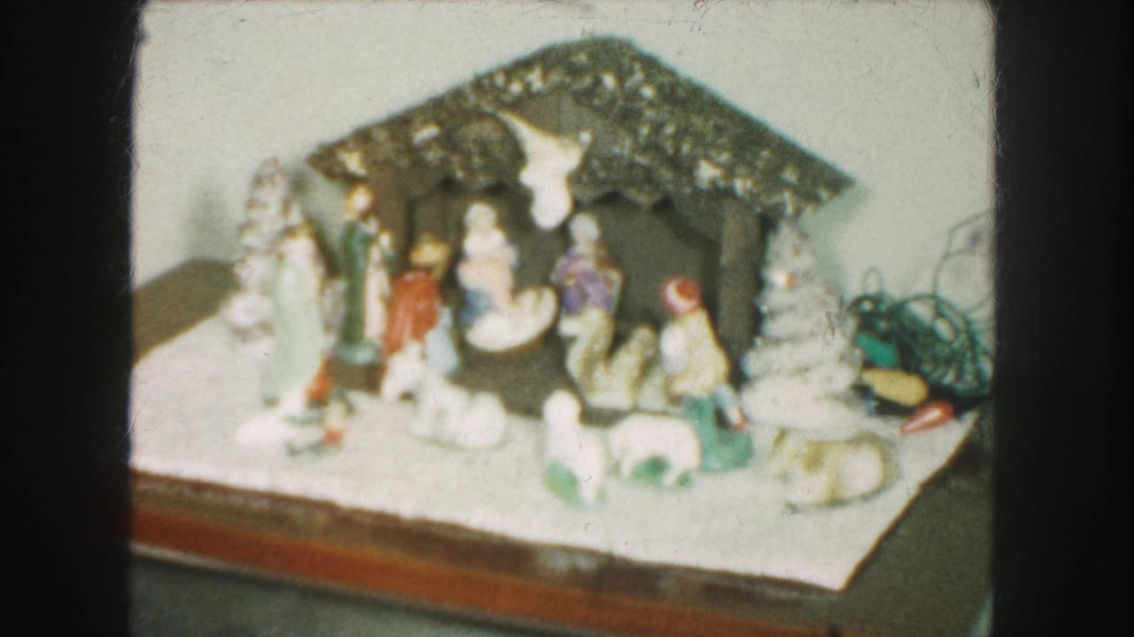 Ceramic nativity scene on a tabletop with small white Christmas trees.