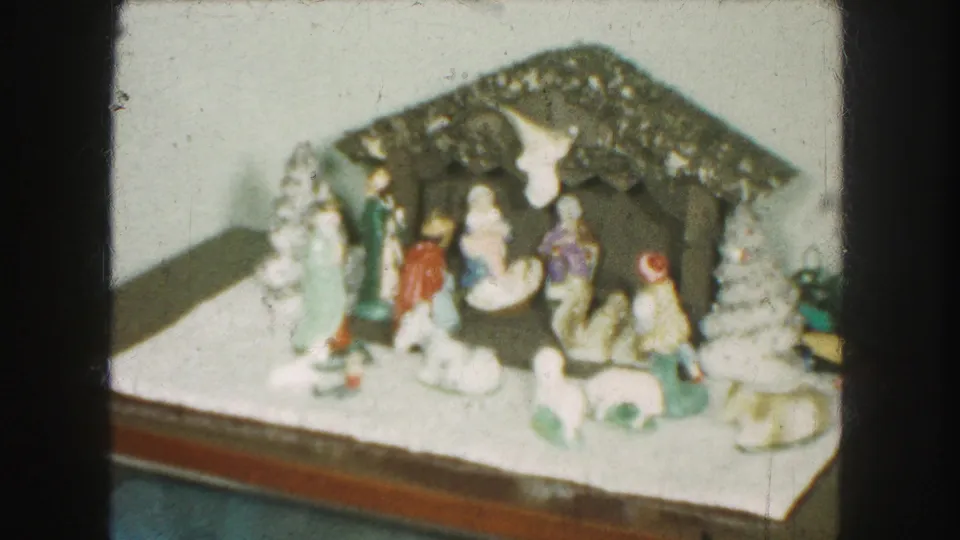 1959 home-movie frame of a ceramic Christmas nativity scene with grouped figures, animals, and white trees on a tabletop.