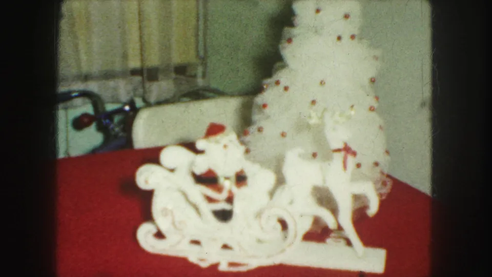 Kansas City 1959 8mm frame showing a white ceramic Santa sleigh with reindeer on a red surface beside a white Christmas tree.