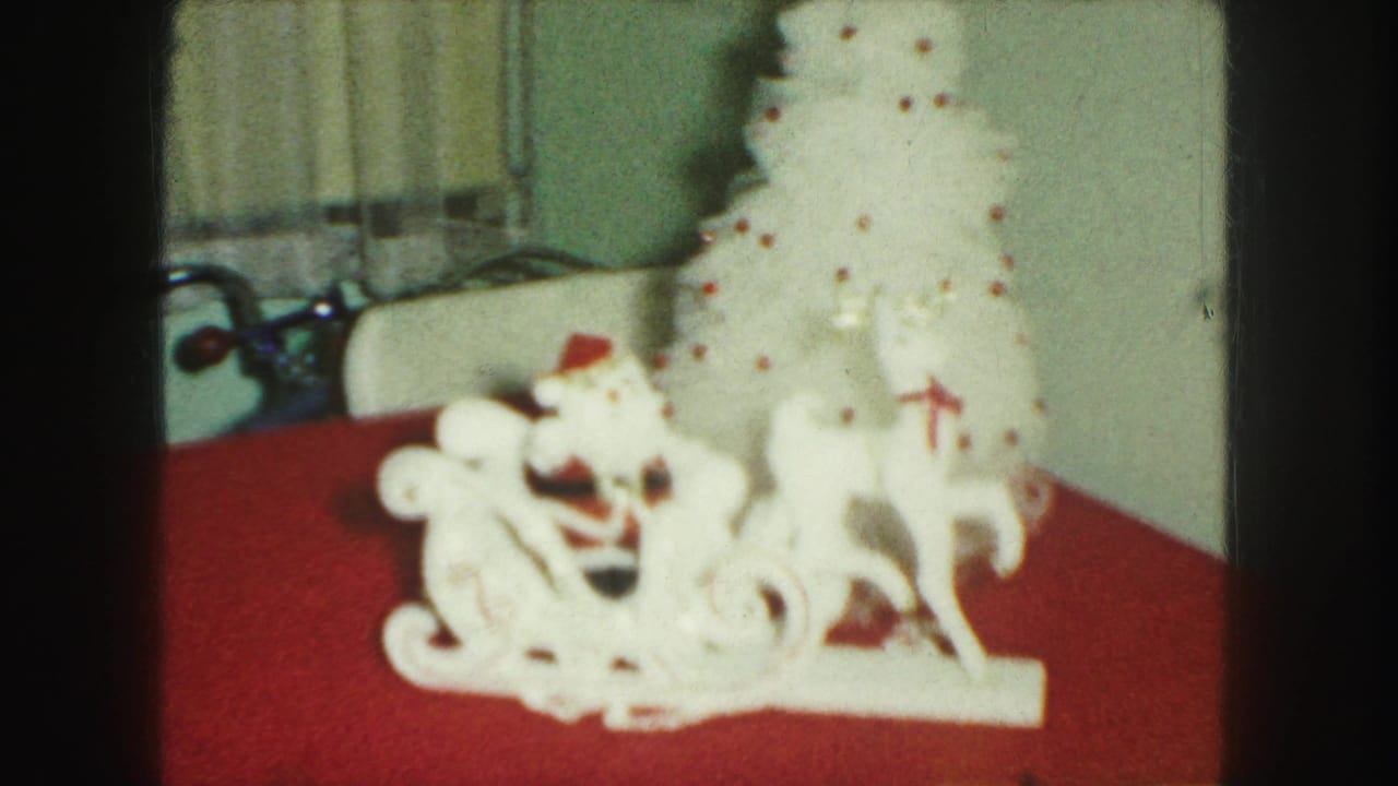 White Santa sleigh, reindeer, and small white Christmas tree on a red tablecloth.