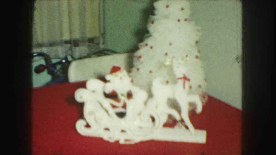 1959 Kansas City 8mm frame showing white tabletop Christmas decorations on a red cloth near curtains and a pale wall.