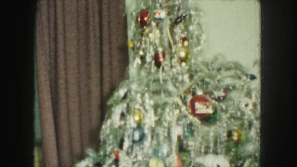 Final Kansas City Christmas interior frame showing the decorated tree with tinsel and ornaments beside curtains and a pale wall.