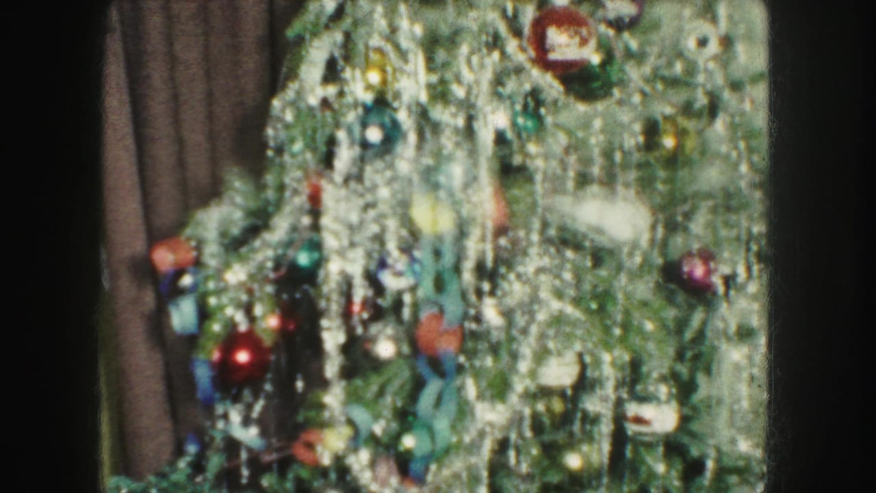 Close view of a tinsel-covered Christmas tree with colorful ornaments beside a dark curtain.
