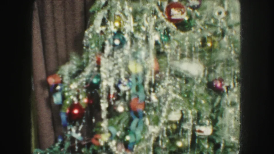 1959 Kansas City home-movie frame showing a decorated Christmas tree with silver tinsel, colored ornaments, and a dark curtain behind it.