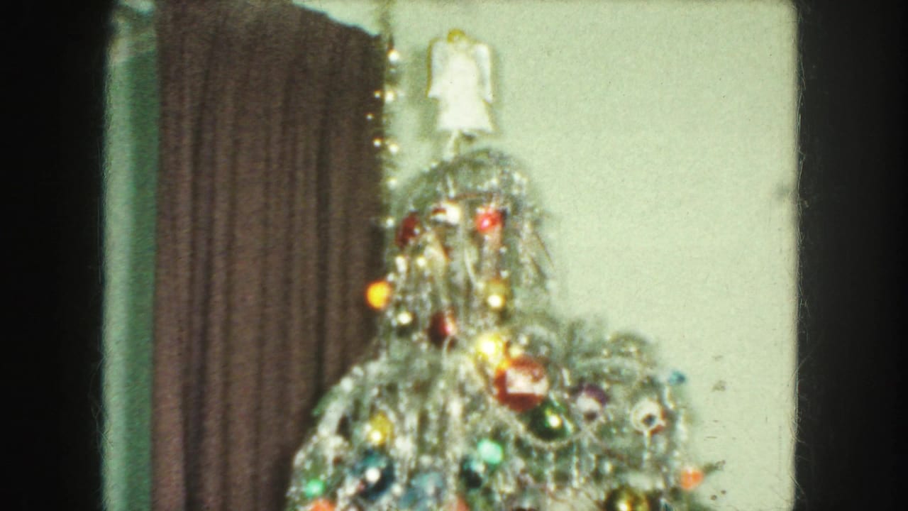 1959 Kansas City frame showing the top of a tinsel-covered Christmas tree with colored baubles, lights, curtain, and wall behind it.