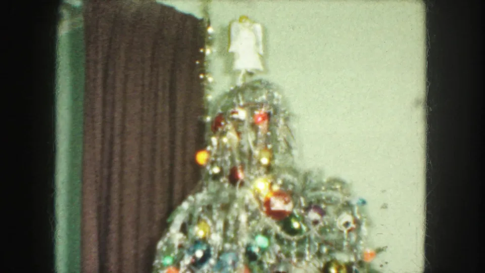 1959 Kansas City frame showing the top of a tinsel-covered Christmas tree with colored baubles, lights, curtain, and wall behind it.