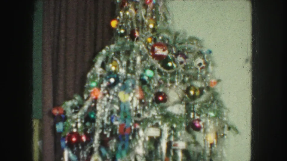 1959 Kansas City home-movie still showing a decorated Christmas tree with dense silver tinsel, glass ornaments, and indoor curtains.