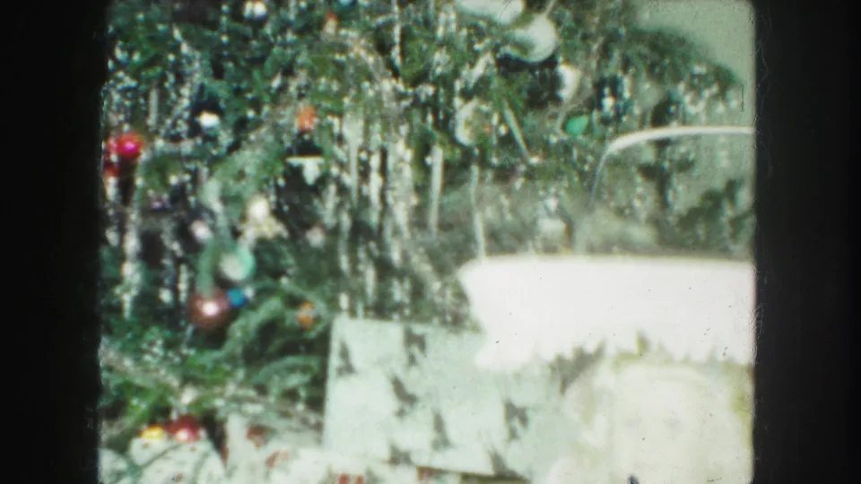 1959 Kansas City frame of a tinsel-covered Christmas tree with ornaments and wrapped presents partly visible below.