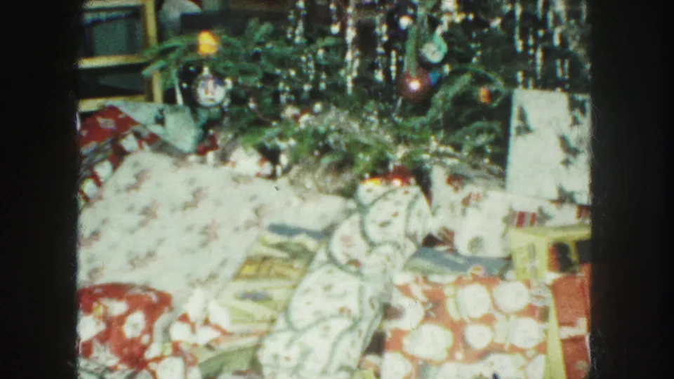 1959 Kansas City frame showing gifts under a decorated Christmas tree, with tinsel, ornaments, and patterned wrapping paper visible.