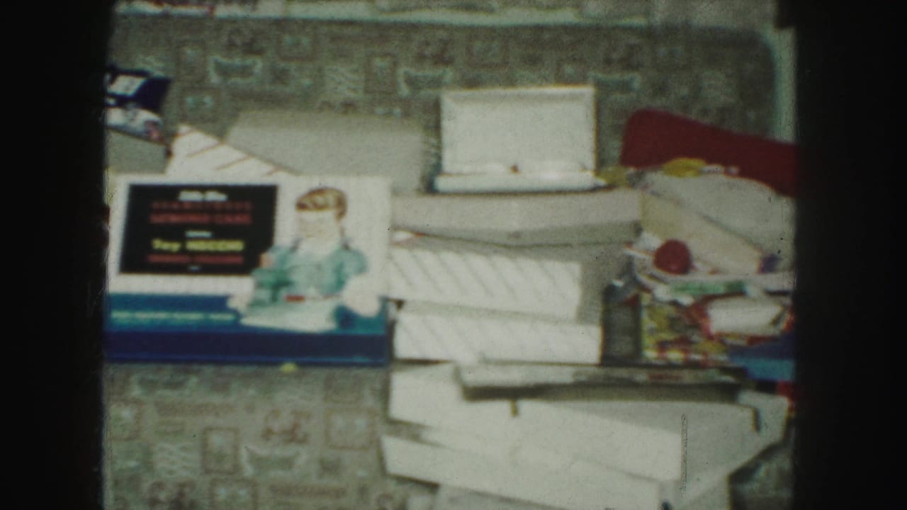 Doll, blue toy box, white cartons, wrapping paper, and colorful packages arranged on a patterned carpet.
