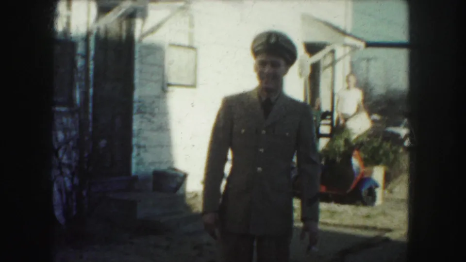 In Kansas City home-movie footage from 1959, a uniformed man faces the camera near a white house and porch.
