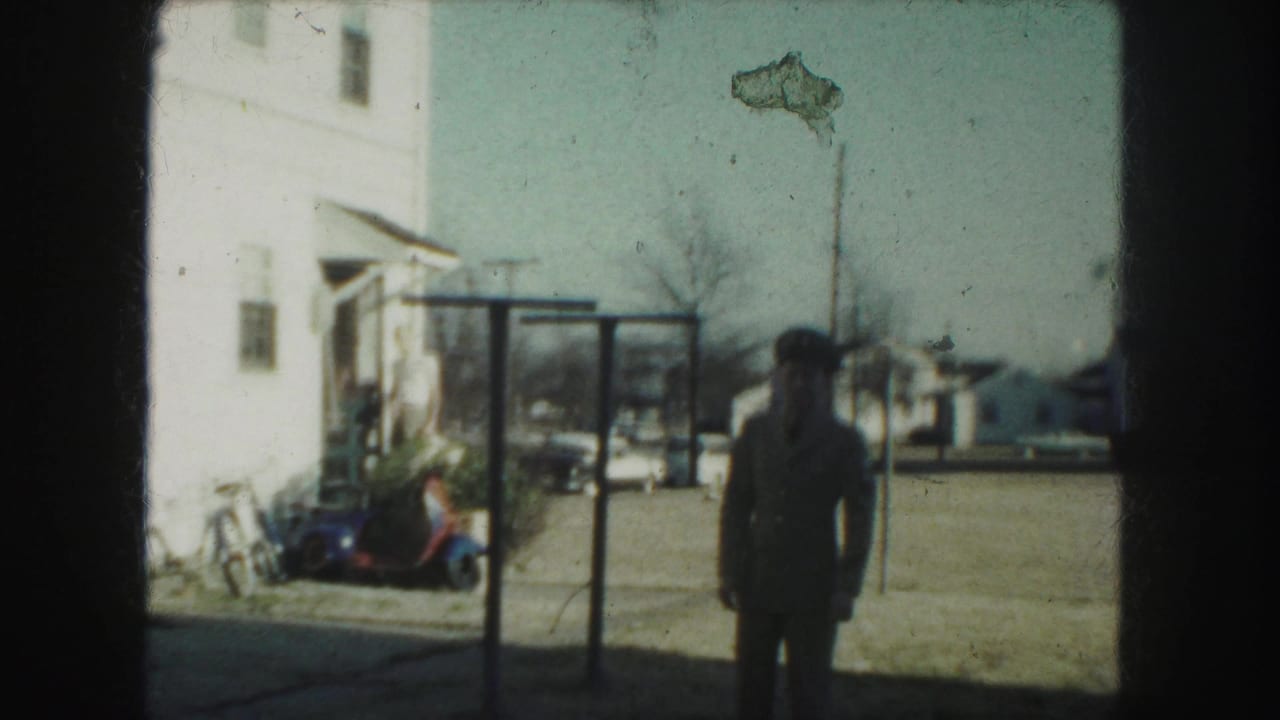 The man in uniform appears farther back in the Kansas City yard, with a white house, scooter, and street visible behind him.