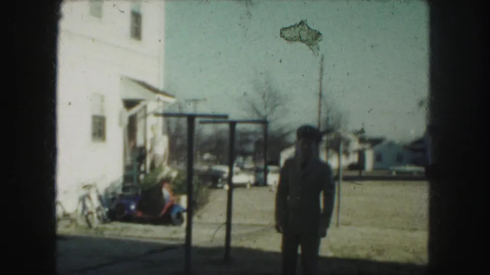 The man in uniform appears farther back in the Kansas City yard, with a white house, scooter, and street visible behind him.