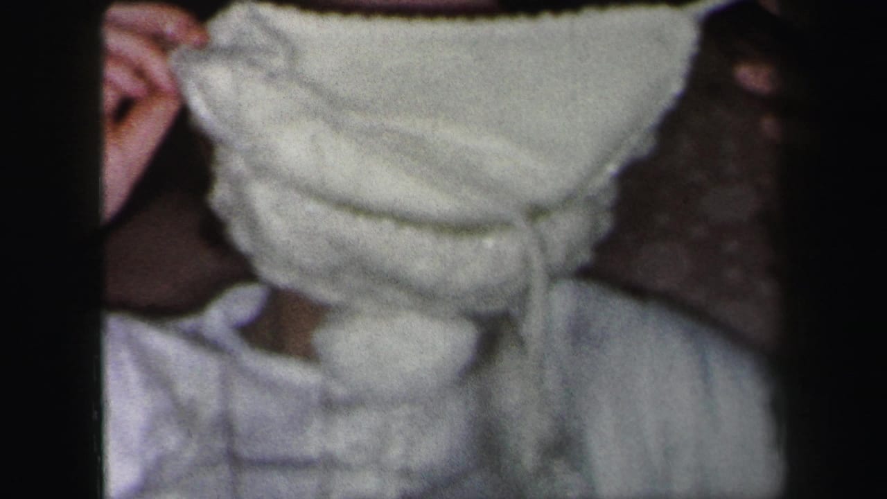 Woman in white clothing holds a white knitted hat across the lower half of her face.