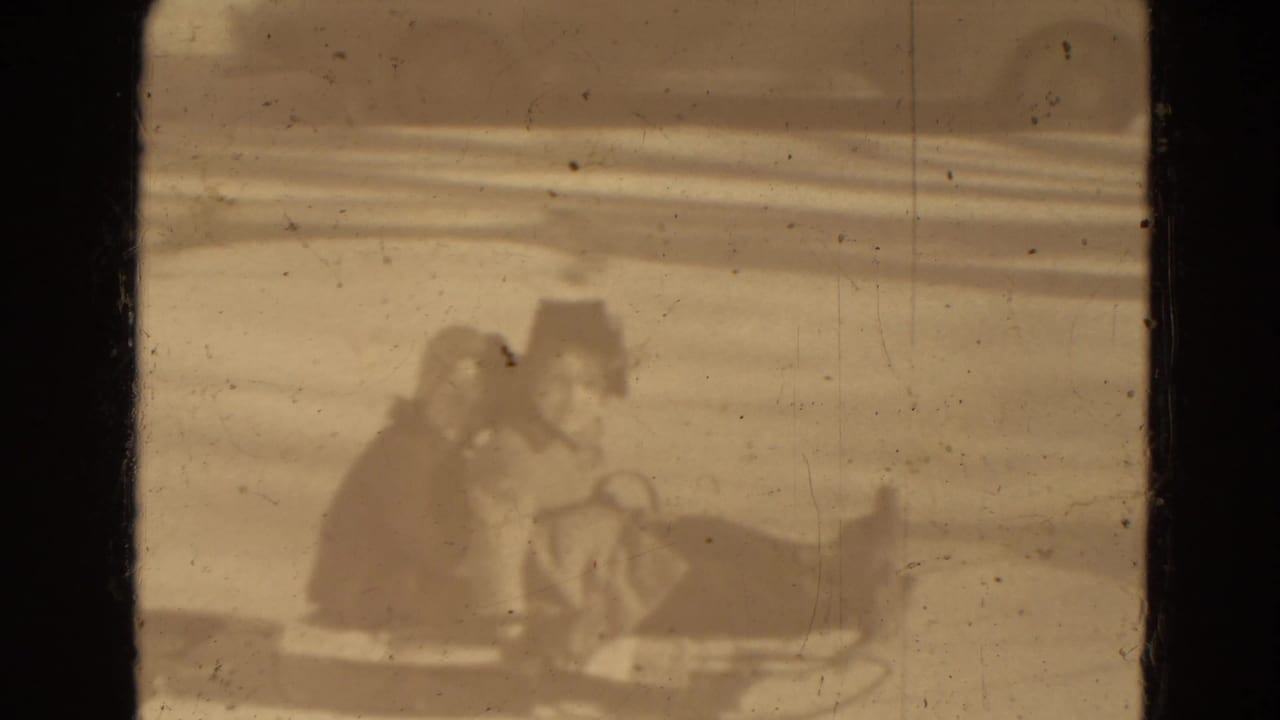 Bundled riders sit on a horse-drawn sleigh or sled crossing snowy ground.