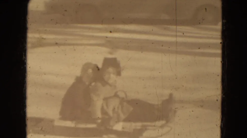 In archival 8mm footage from Lincoln, Nebraska, bundled riders appear on a horse-drawn sleigh or sled moving through snow.