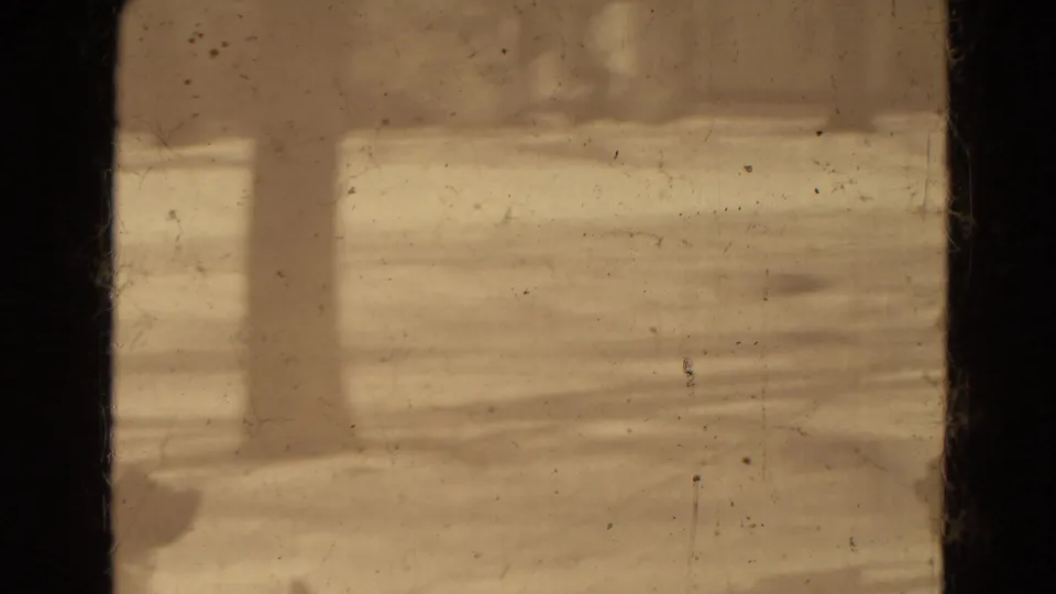 A foreground figure stands near the camera while the snowy 8mm scene continues, with soft focus and visible film wear obscuring details.