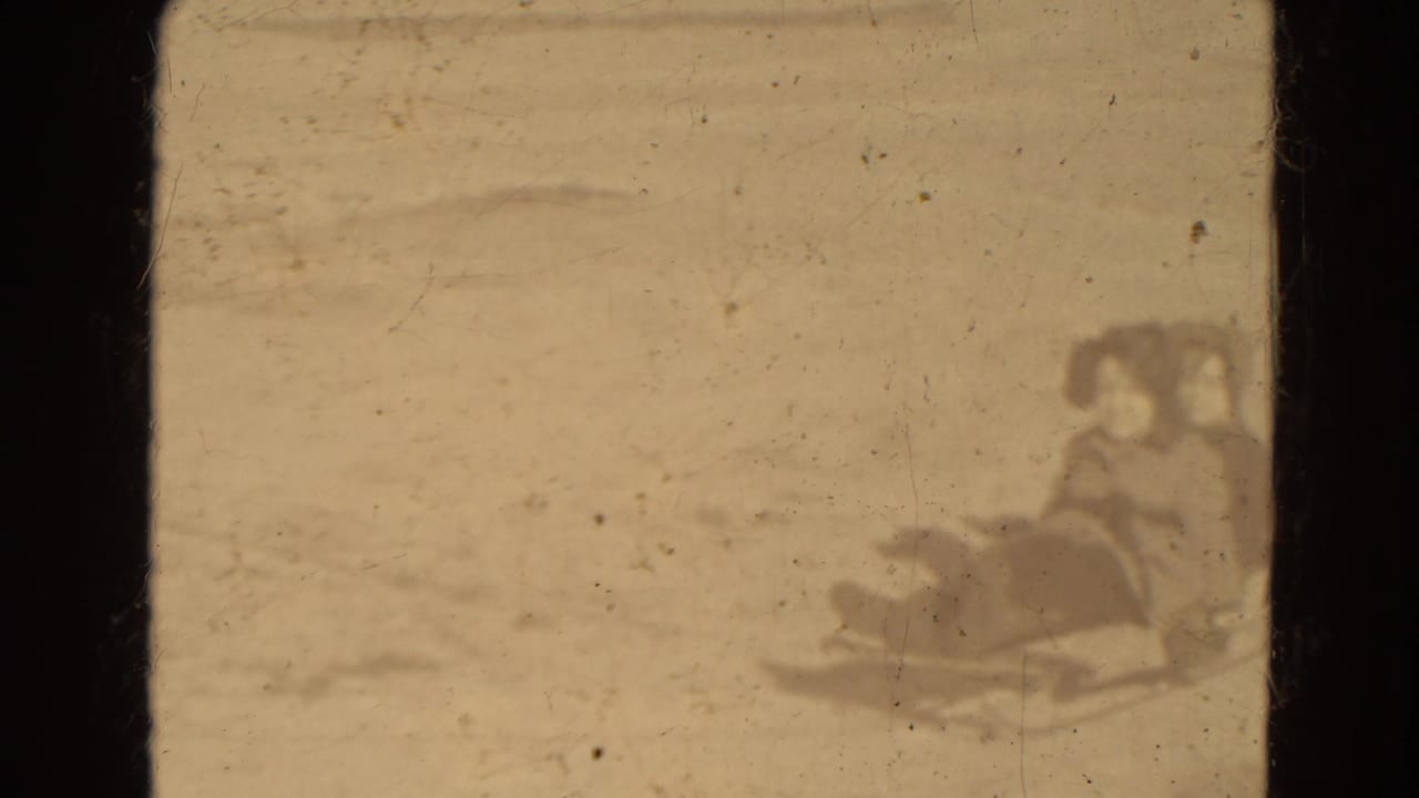 Bundled figures on or near a sled crossing a snowy area in soft focus.
