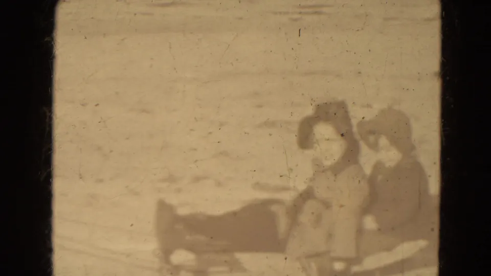 Soft 8mm home-movie frame showing two bundled young people seated on or beside a sled in Lincoln, Nebraska.