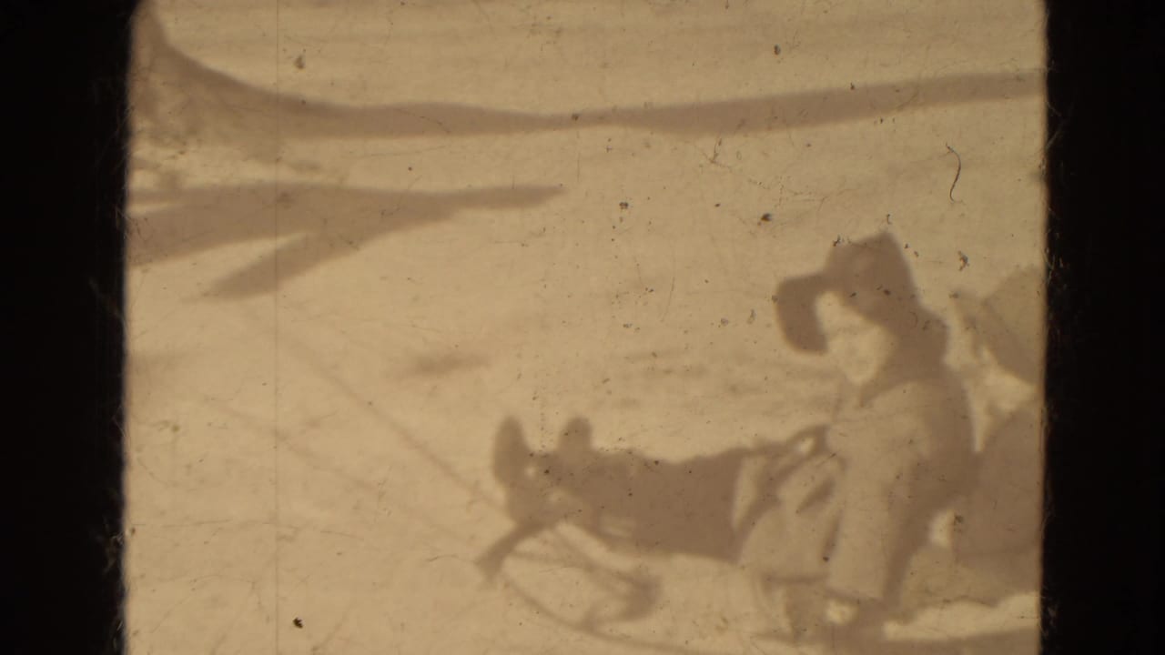 Two distant bundled figures appear with a sled on snowy ground in 1942 Lincoln, Nebraska home-movie footage.