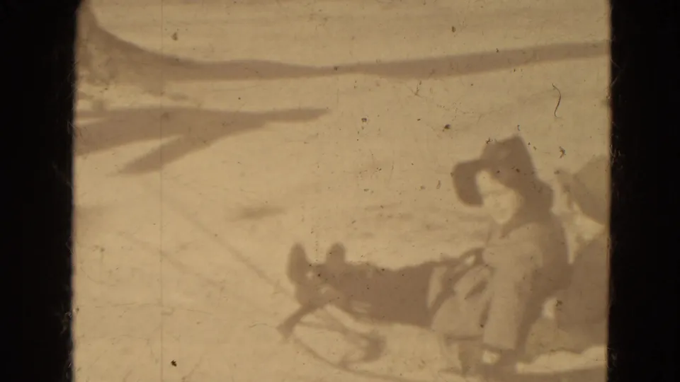 Two distant bundled figures appear with a sled on snowy ground in 1942 Lincoln, Nebraska home-movie footage.