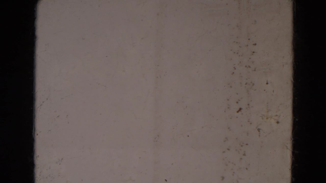 Static blank 8mm frame from the supplied Lincoln, Nebraska metadata, with pale exposure, dust specks, surface marks, and black frame dividers.