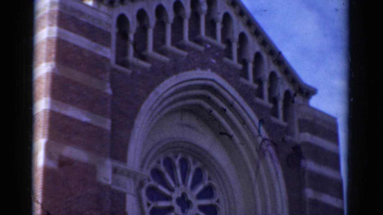 1975 Bridgeport home-movie frame showing the upper brick facade of a church with Gothic-style arches and a partial rose window.