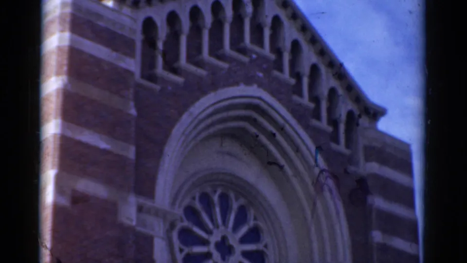 1975 Bridgeport home-movie frame showing the upper brick facade of a church with Gothic-style arches and a partial rose window.