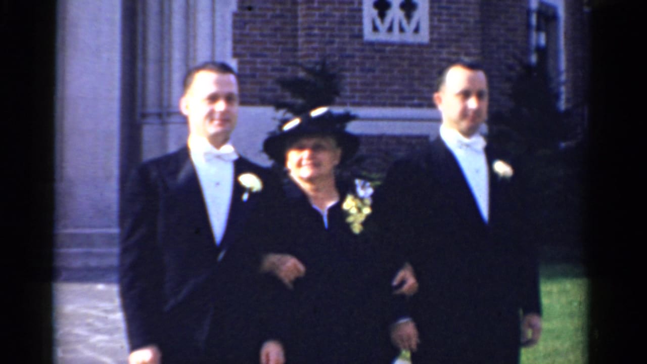 Two men in tuxedos stand with an older woman in a dark hat outside a brick church.