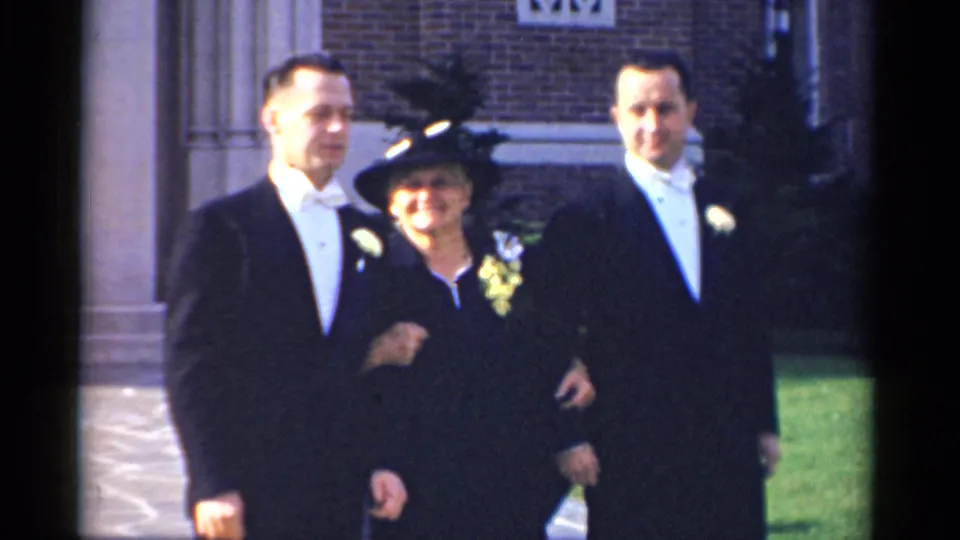1975 Bridgeport home-movie frame of the wedding group still posing outside the brick church, with soft color and visible film gate edges.