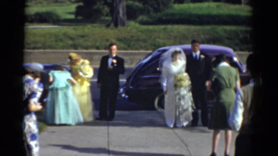 The 1975 Bridgeport wedding group stands outdoors with the bride and groom near a purple car and attendants in pastel dresses nearby.