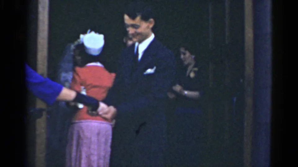 1975 Bridgeport wedding footage shows a groom near formally dressed guests at a building entrance.