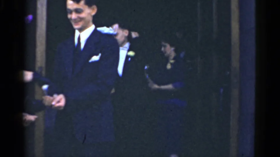 1975 Bridgeport wedding scene with a smiling groom in a dark suit and guests in formal clothing behind him.