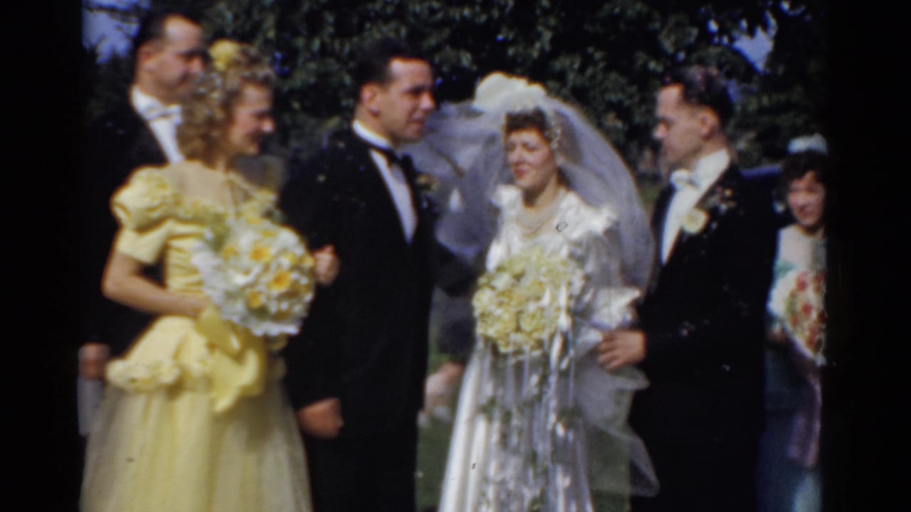 Bride and groom stand outdoors with wedding party members holding bouquets.