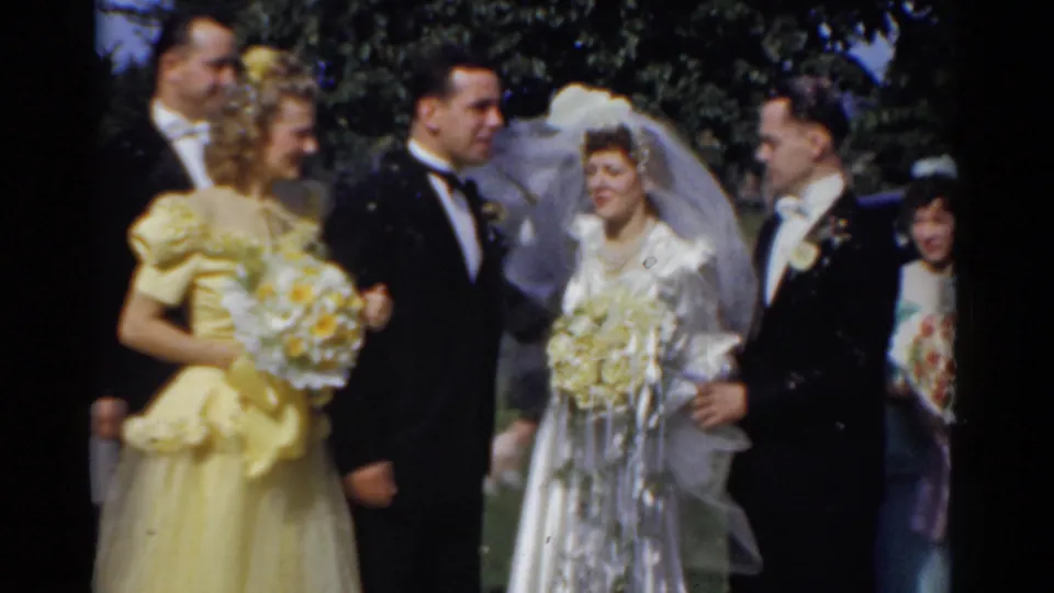 1975 Bridgeport wedding party outdoors with bride in veil, groom in tuxedo, bridesmaid in yellow, and guests posed under trees.