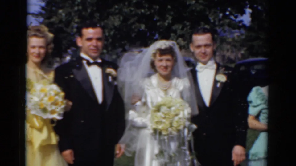 1975 Bridgeport wedding group outdoors, with the bride centered between tuxedoed men and attendants partly framed at the edges.